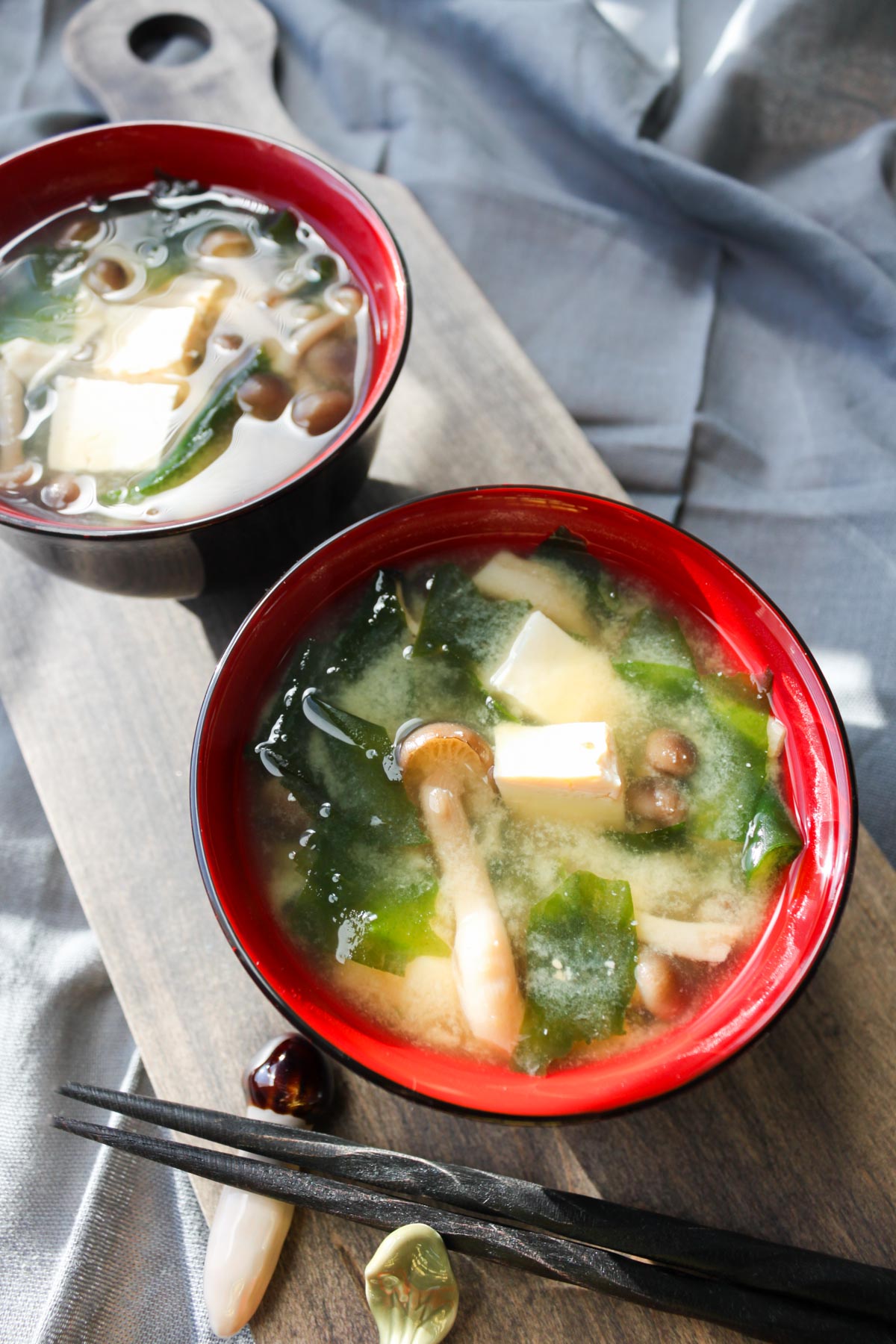 two bowls of miso soup on a wood tray with two sets of chopsticks.