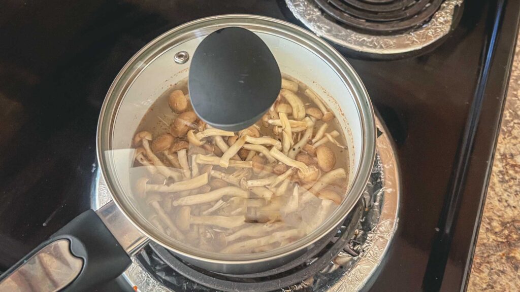 dashi and shimeji mushrooms in a pot on a gas stove with a lid on.