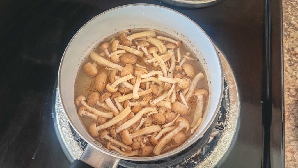 dashi and shimeji mushrooms in a pot on a gas stove.