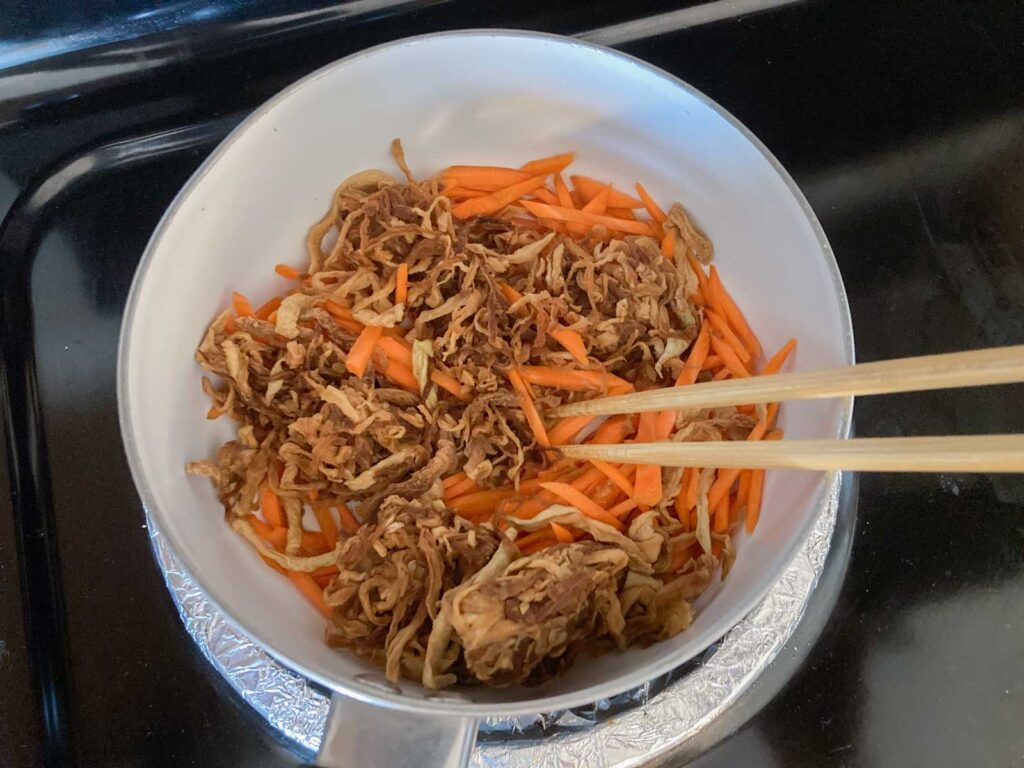 kiriboshi daikon and julienned carrots are being fried in a pot with chopsticks