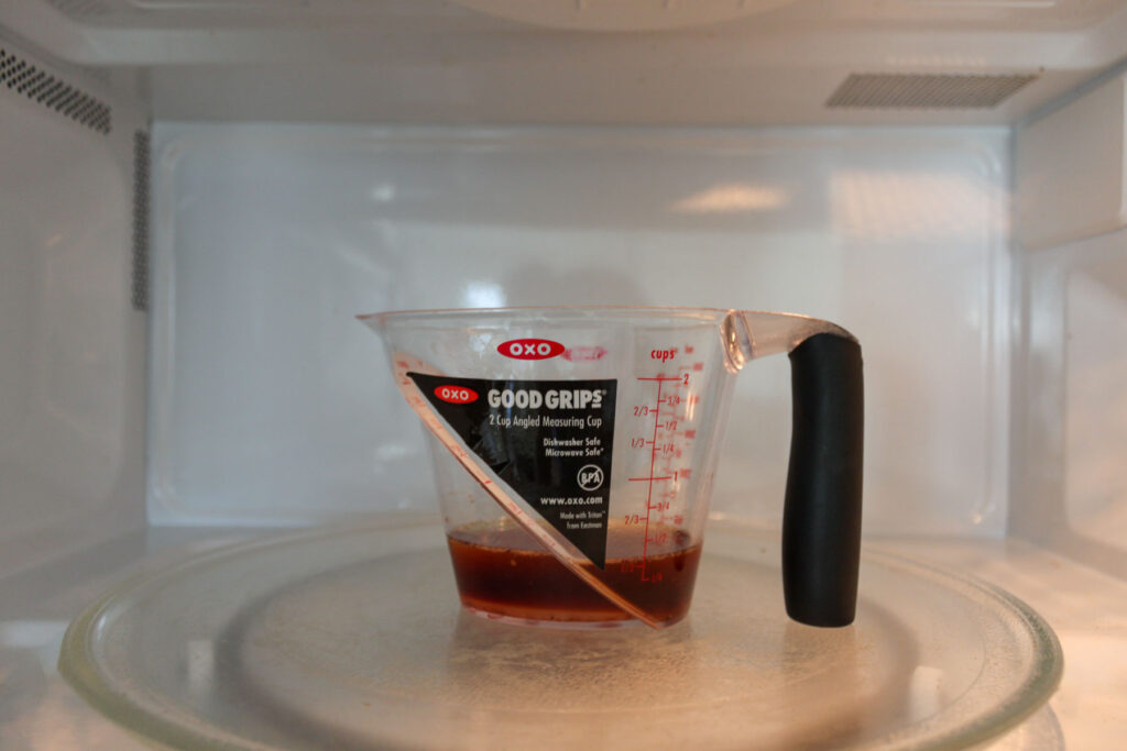 a measurement cup with liquid in it, and it's in a microwave.