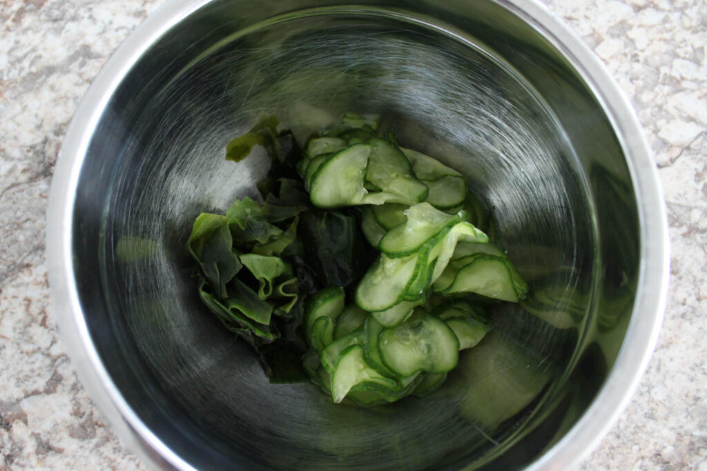 a bowl with squeezed cut wakame and sliced cucumbers in it.