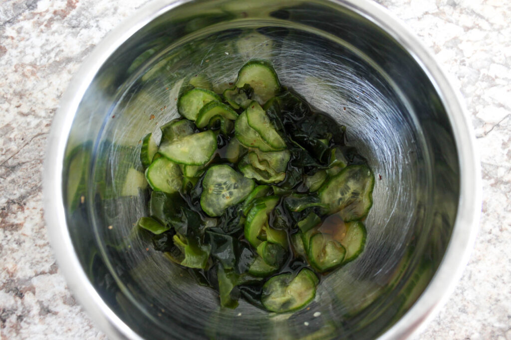 a bowl with sliced cucumbers, cut wakame, and dressing.