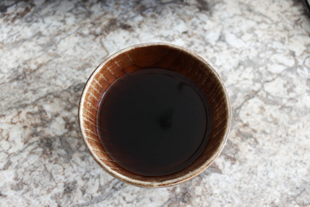 a dark liquid, teriyaki sauce, is in a small wooden bowl.