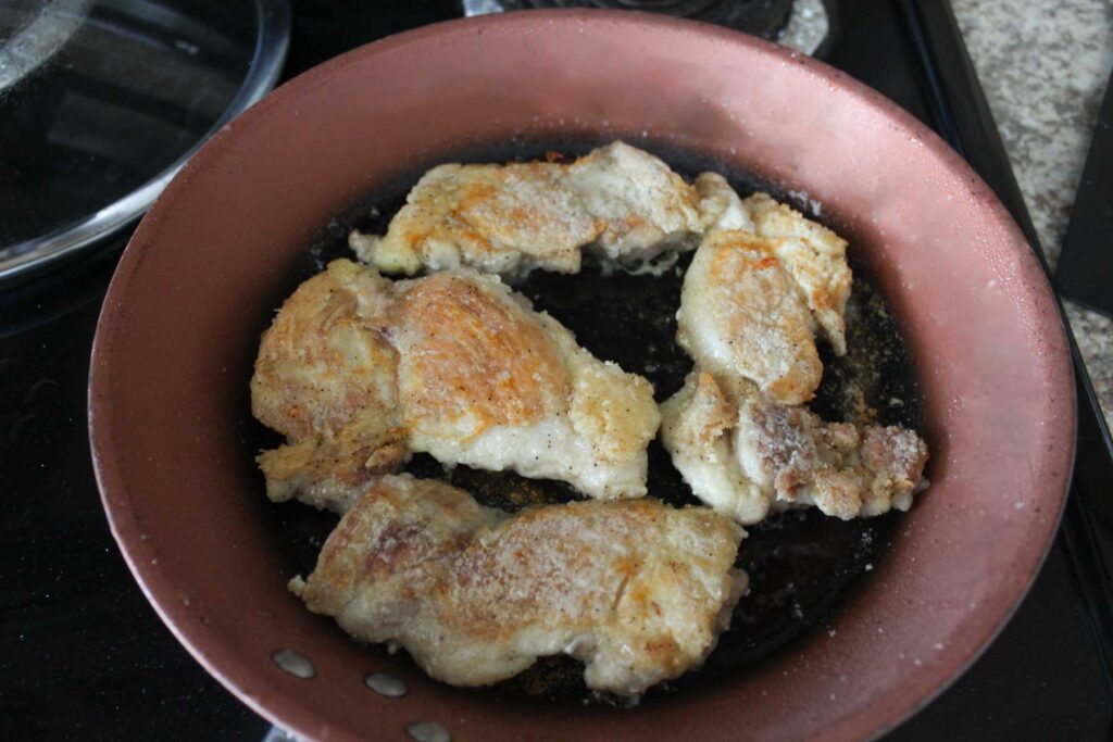 four chicken thighs on a frying pan, and the upper side is golden brown.