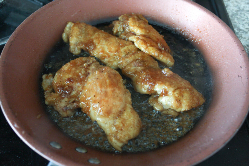 four chicken thighs and teriyaki sauce on a frying pan.