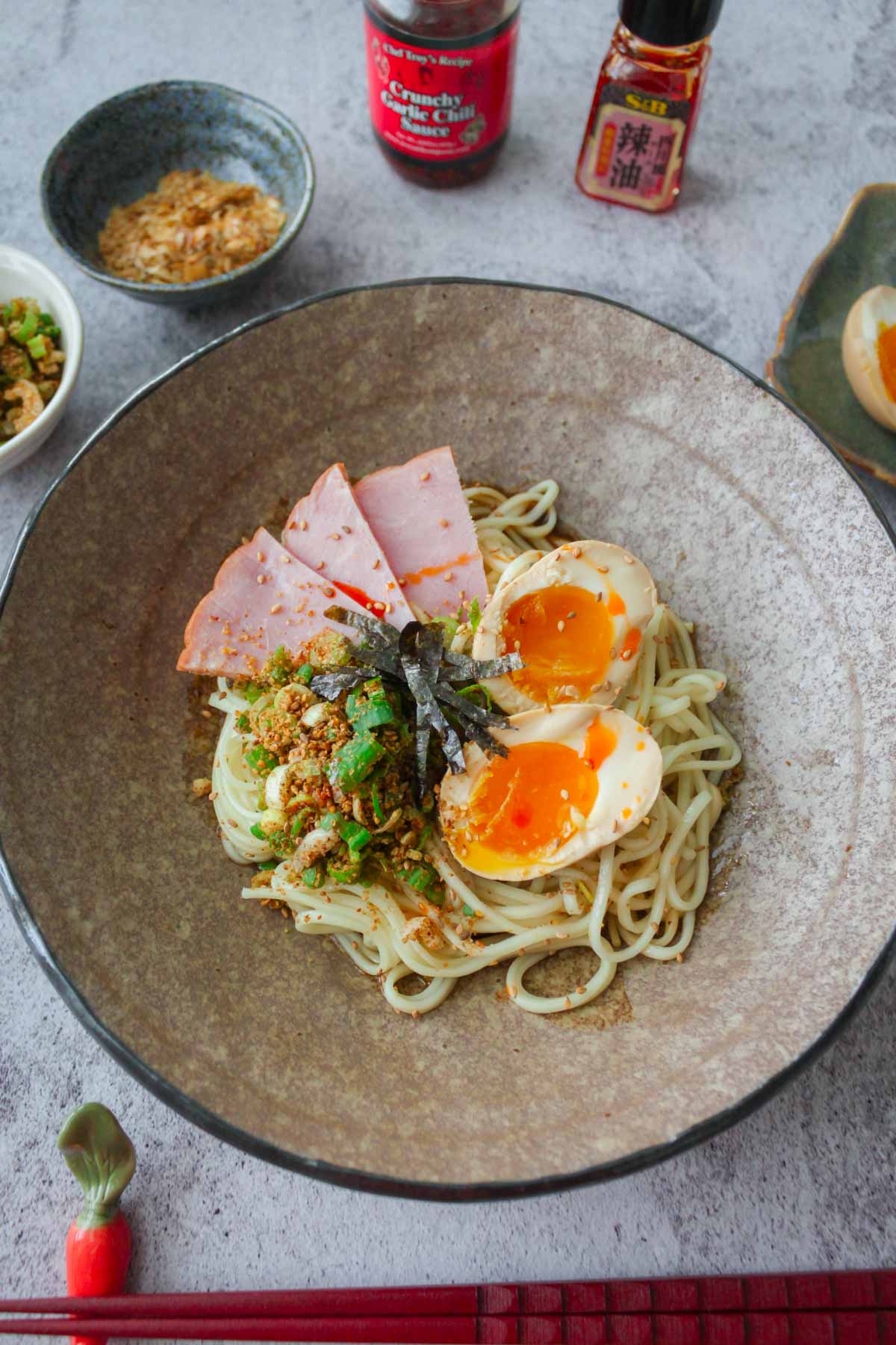 abura soba in a bowl topped with ajitama, nori, ground sesame and scallions, and sliced pork ham