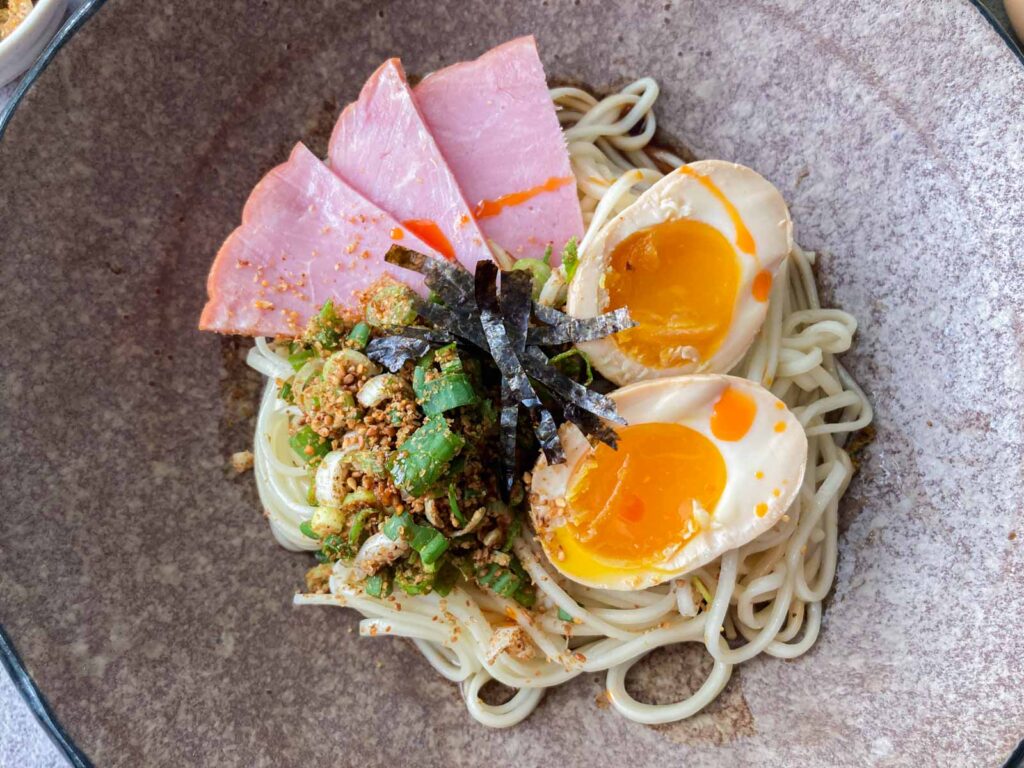 abura soba in a bowl topped with ajitama, nori, ground sesame and scallions, and sliced pork ham