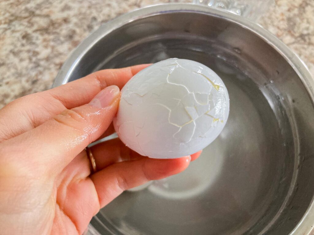 a hand is holding a boiled egg with cracks on the shell