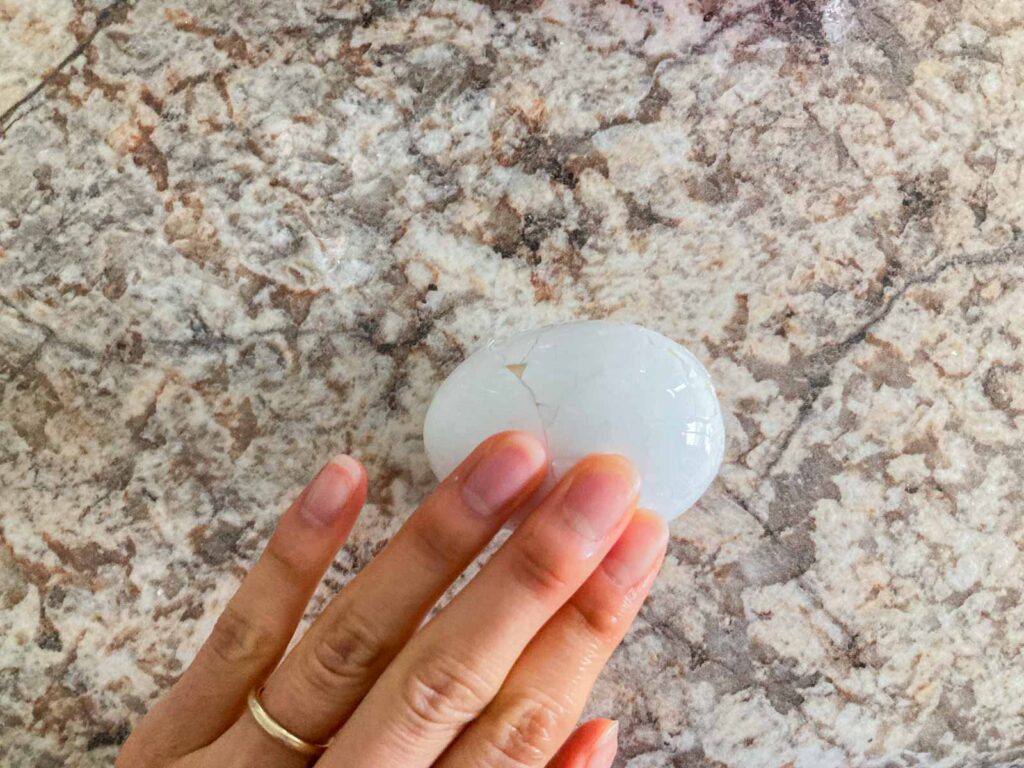 a hand is rolling a boiled egg on a counter to make cracks on the shell