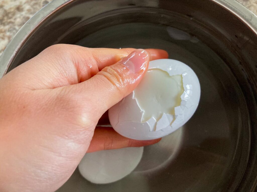 a hand is holding a boiled egg with cracks on the surface, and the thump is trying to peel the shell