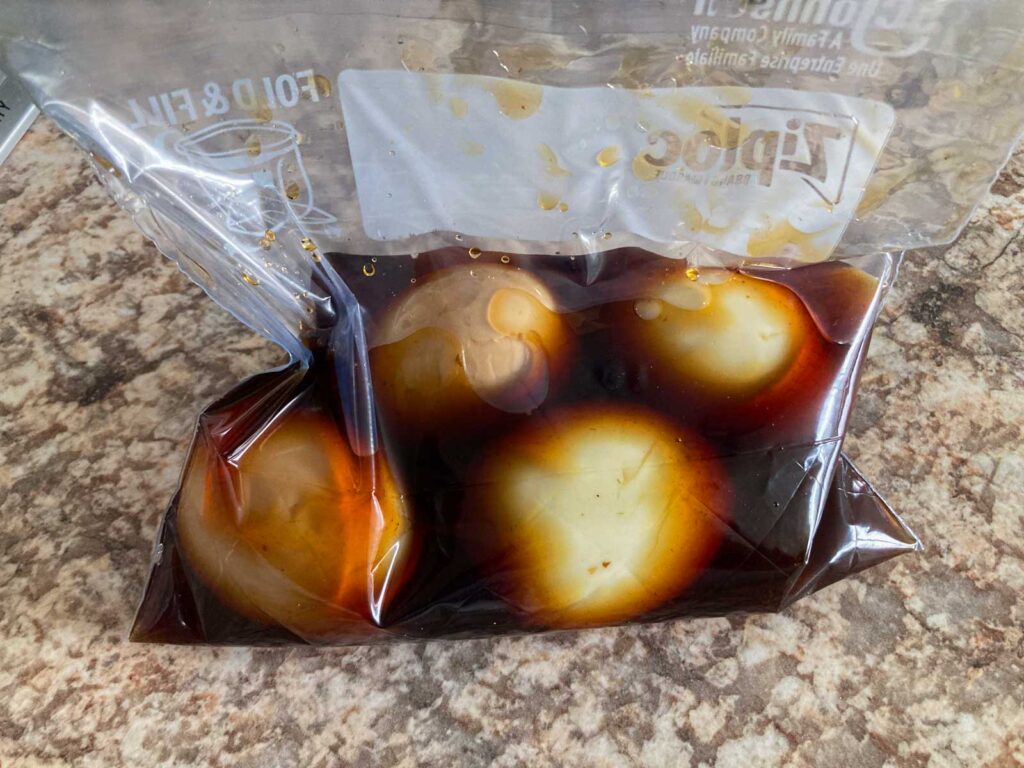 four boiled eggs are marinated in soy sauce based marinade in a plastic bag