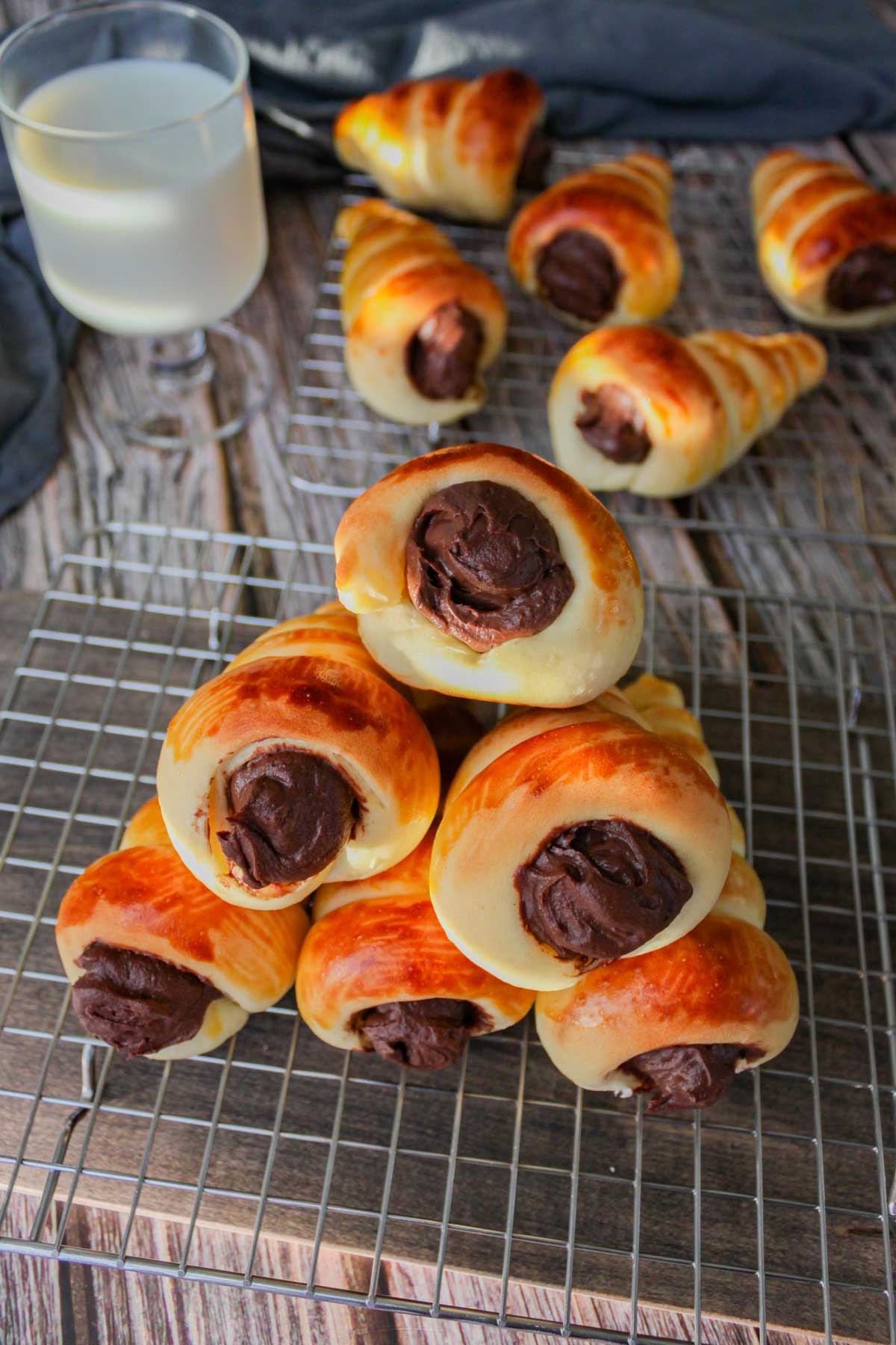 six chocolate coronets on a cooling rack, a glass of milk, and five more chocolate coronets behind