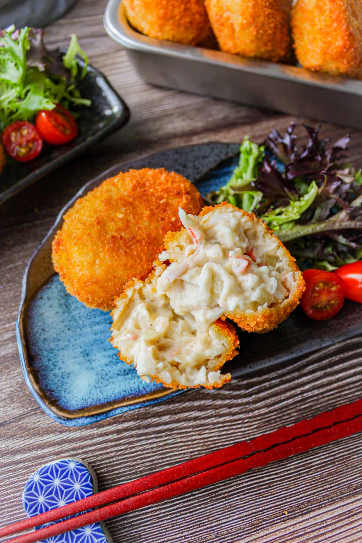 two creamy crab croquettes, one of them is cut into half to show the white sauce inside, on a plate with salad