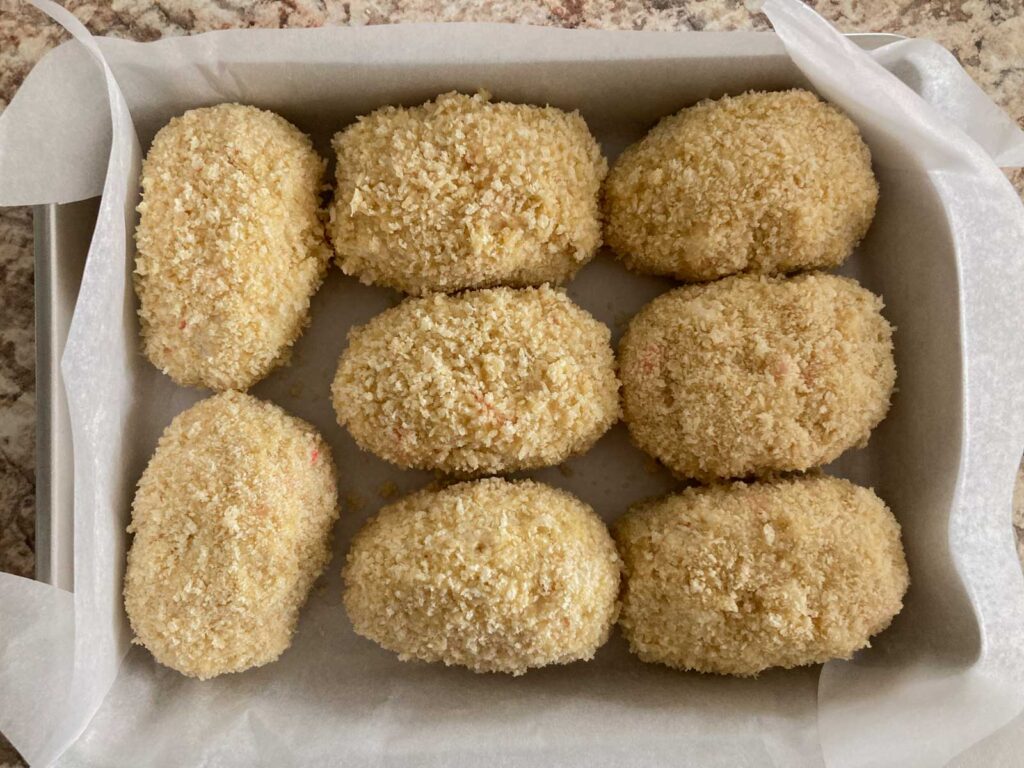 eight creamy crab croquettes breaded and laid in a food tray over parchment paper