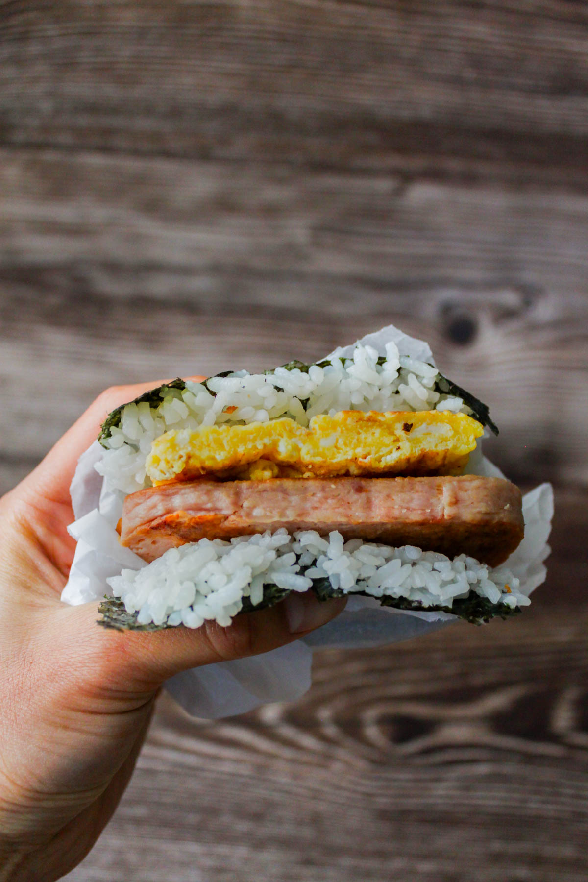 a hand is holding a spam musubi with egg