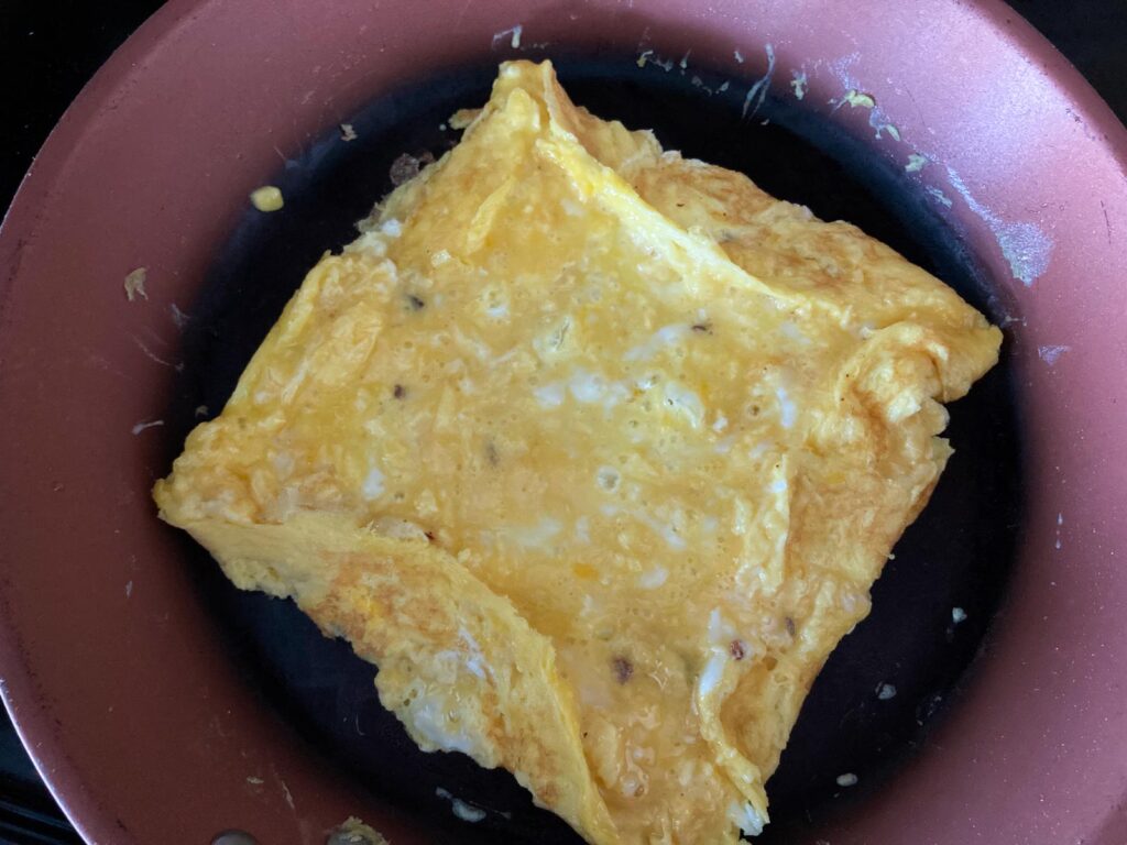 flat egg omelet is fried in a pan, the edges are folded into the center to create a square omelet