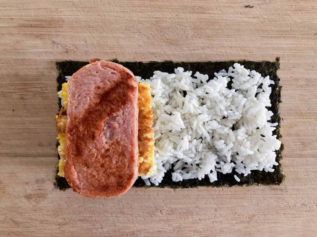 nori seaweed, white rice, egg, and spam on a cutting board