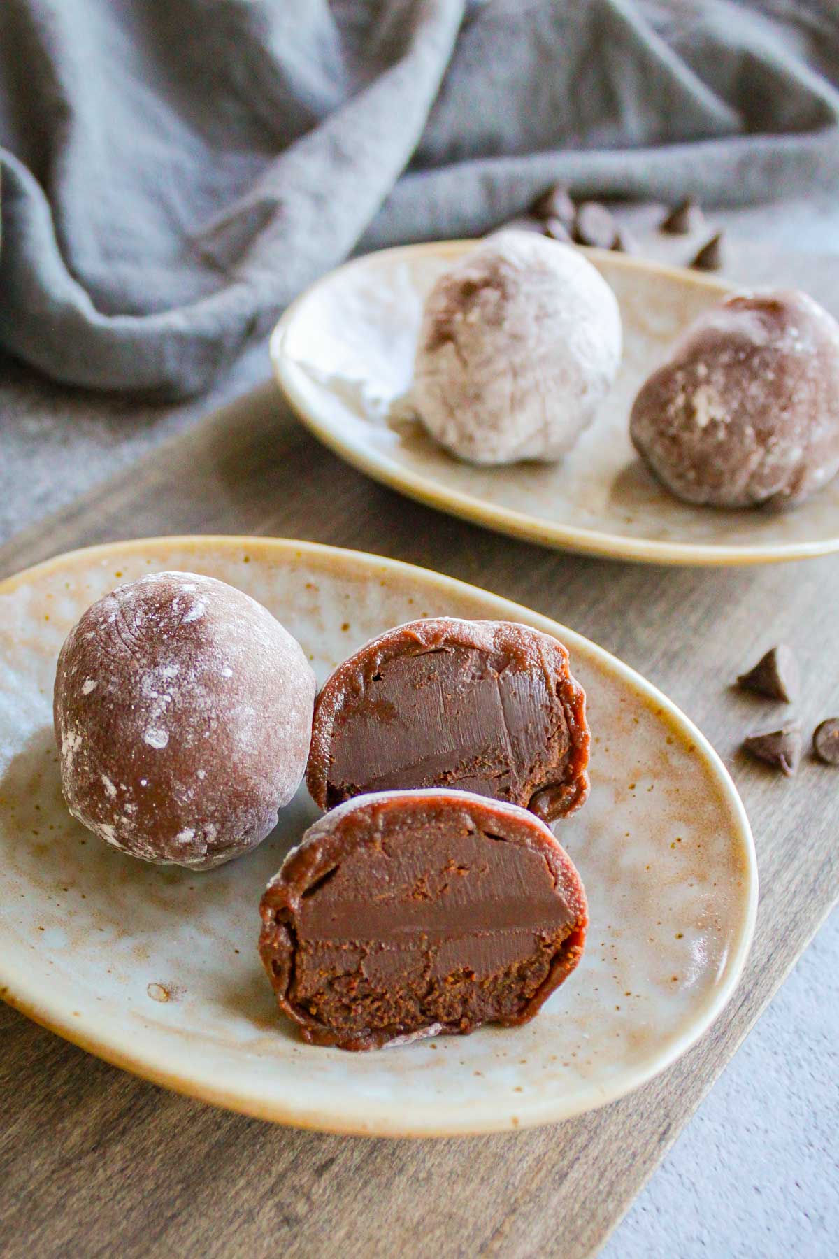 two chocolate mochi on a plate, one of them is cut into half