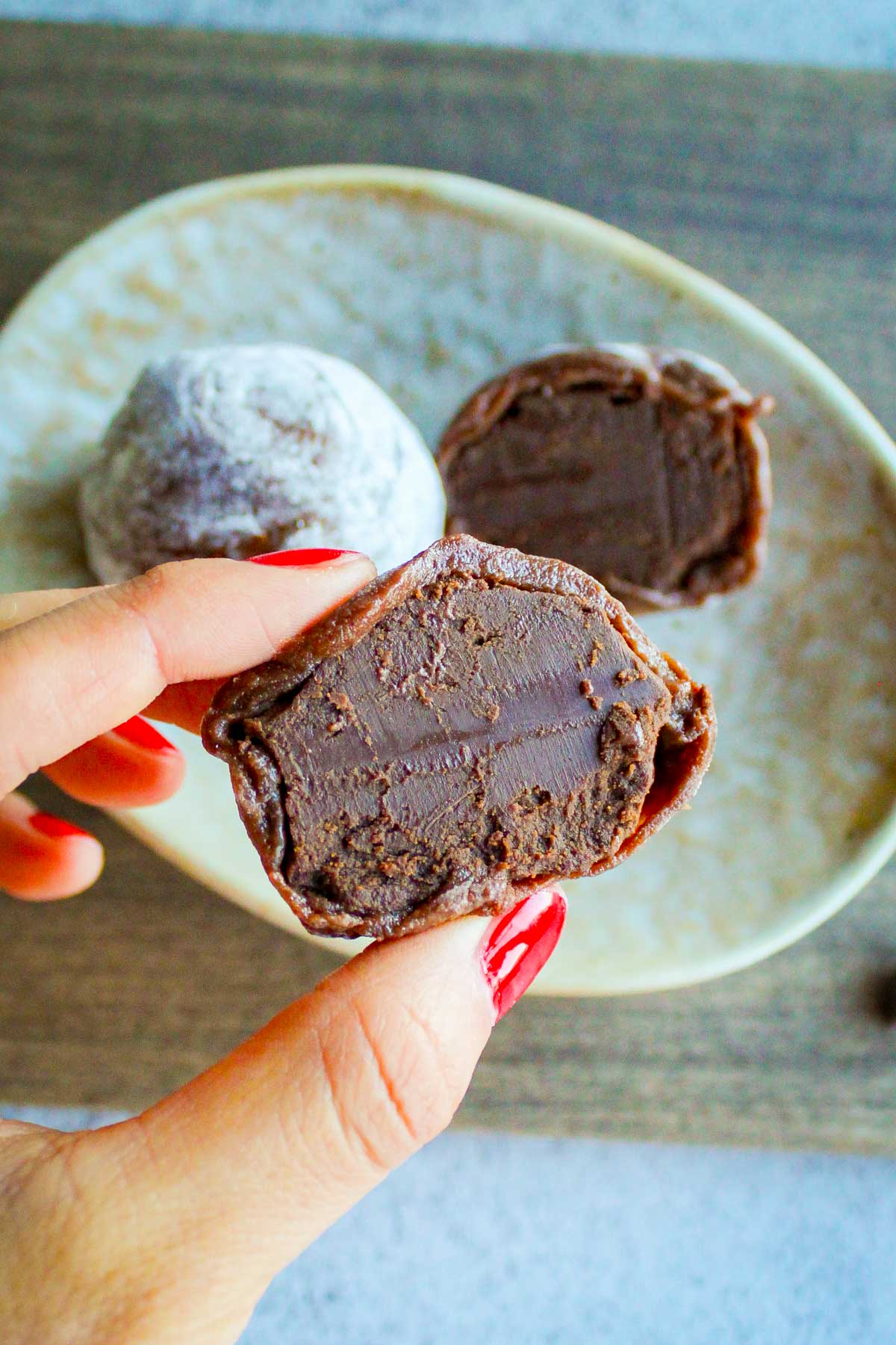 a hand holding a chocolate mochi cut into half