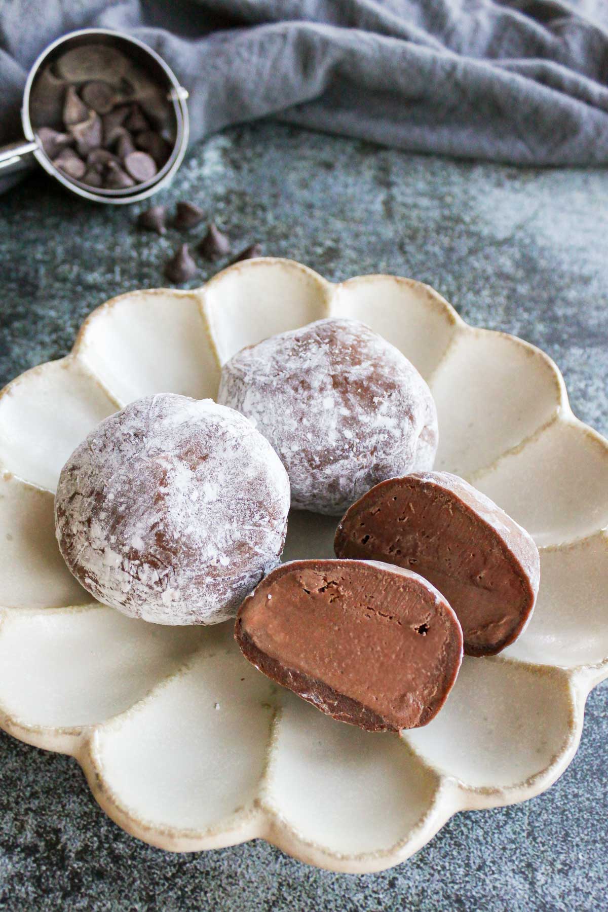 three chocolate mochi ice cream on a plate, one of them is cut into half