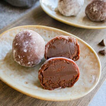 Two chocolate mochi with ganache on a plate.