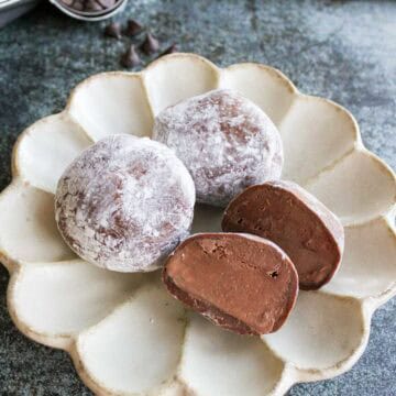 Three chocolate mochi ice cream, one of them is cut into half on a plate.