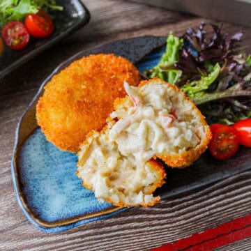Two creamy crab croquettes on a plate, one is cut into half.