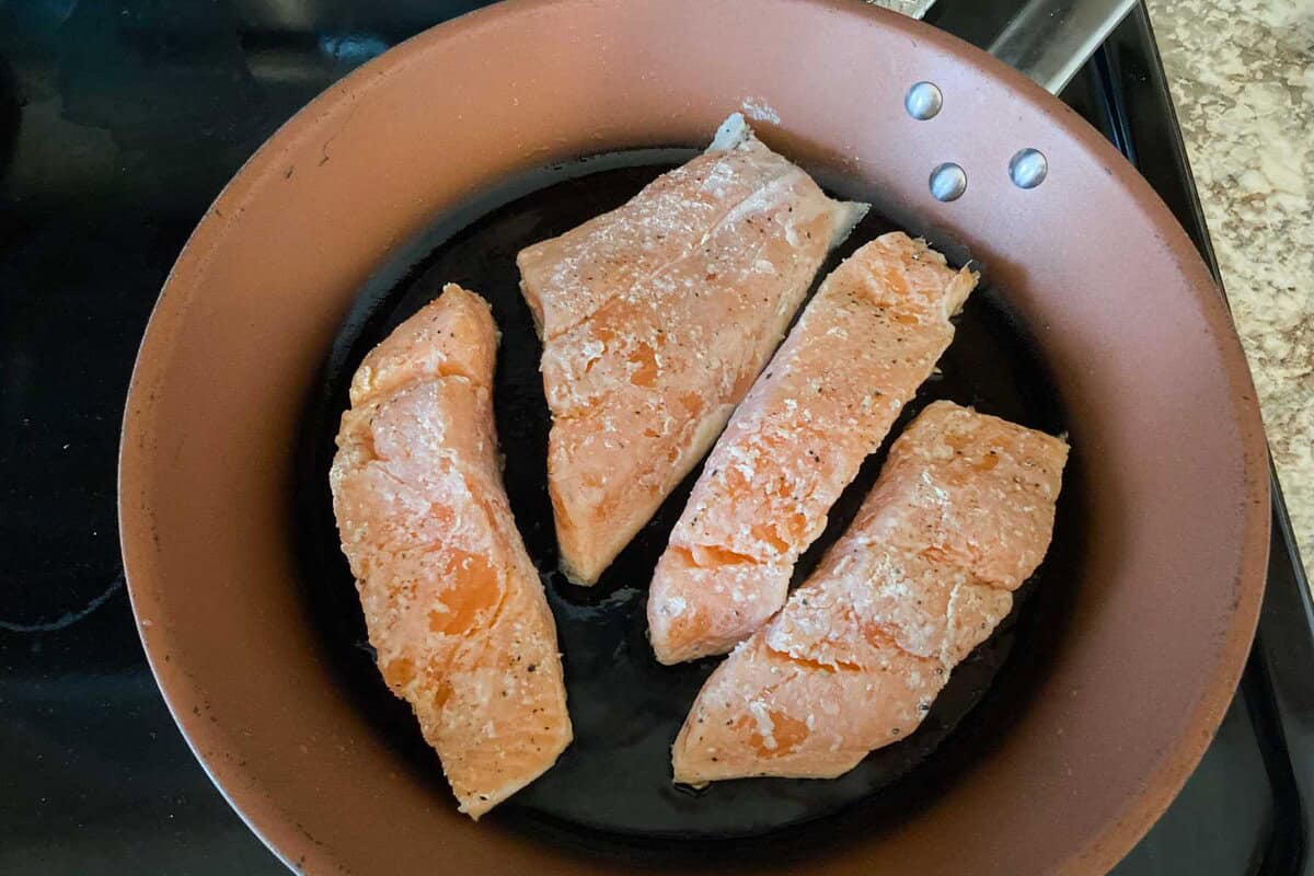 slices of salmon are fried on a pan.