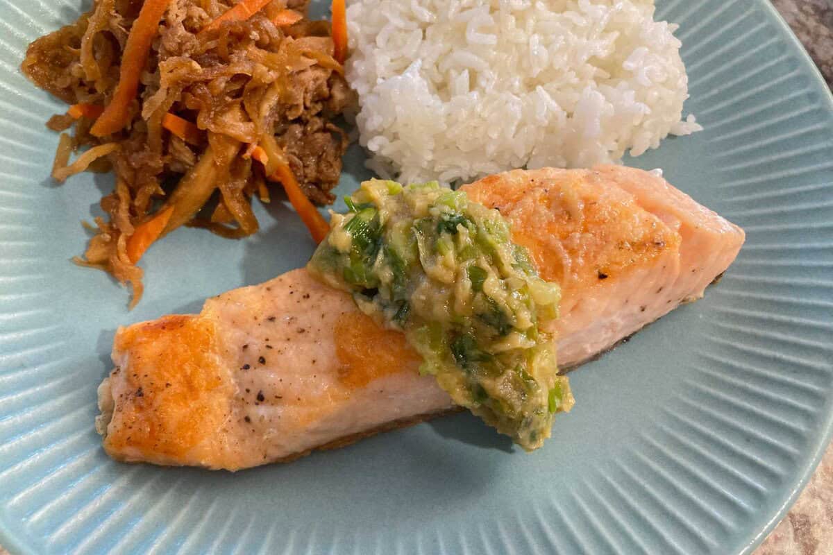 Baked salmon topped with miso butter scallion sauce on a plate.