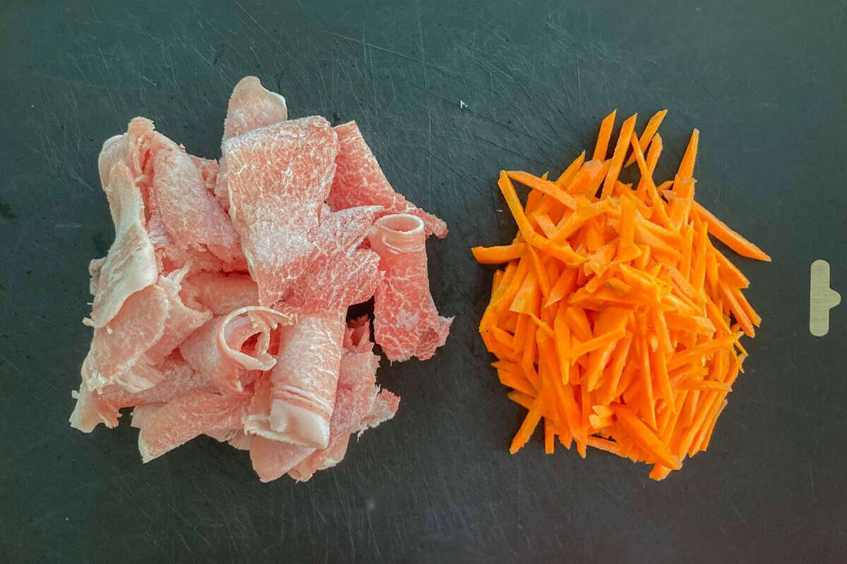 sliced pork and striped carrots on a cutting board.