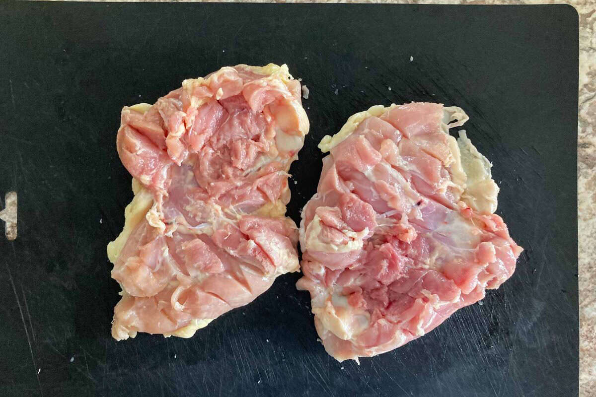 Two pieces of chicken thighs on a cutting board.