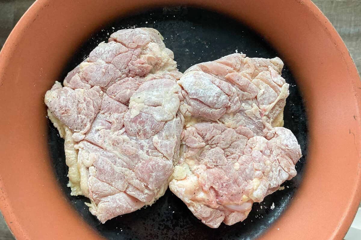 Two pieces of chicken are on a pan skin side down.