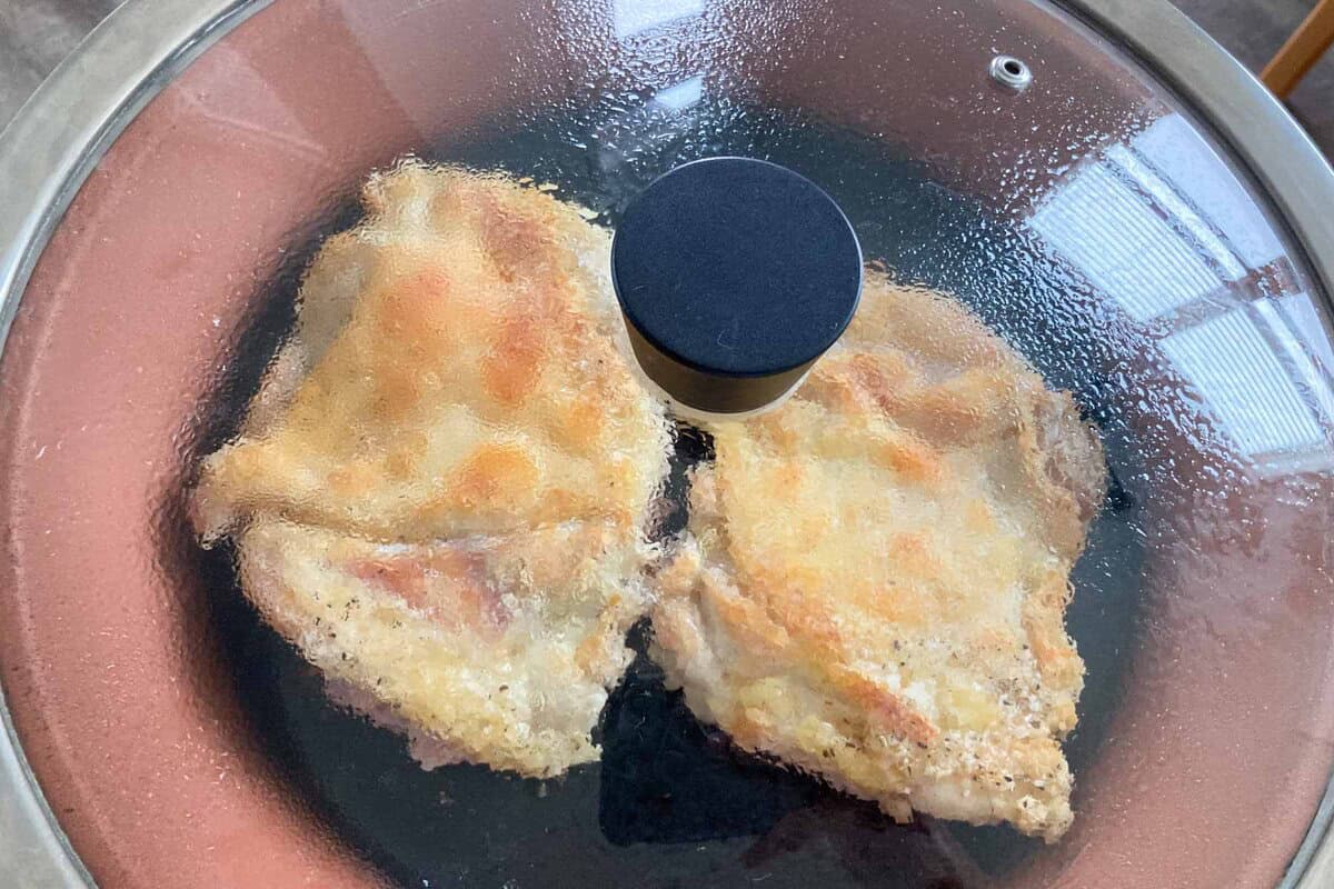 Two pieces of chicken are steamed in a pan with a lid on.