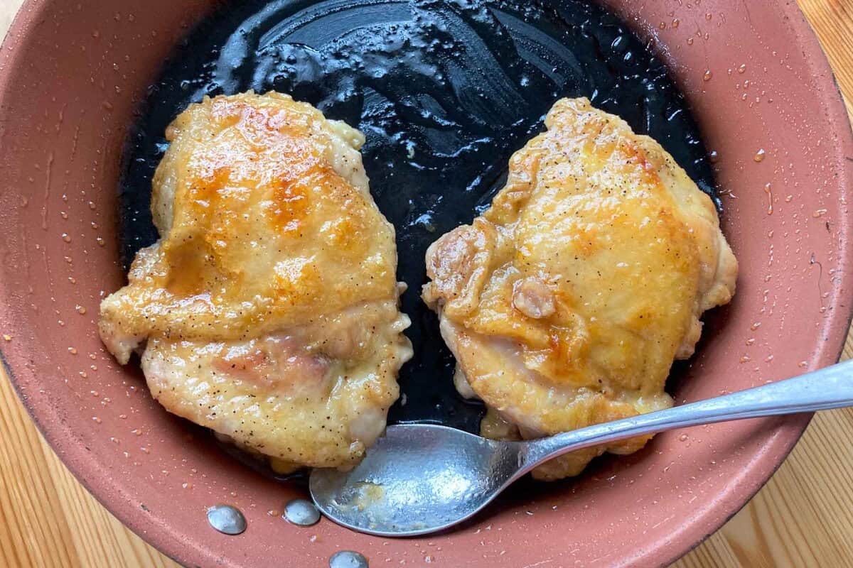 Two pieces of chicken coated in teriyaki sauce on a pan.