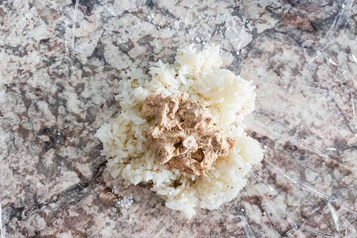 Tuna mayo mixture on top of rice on a plastic wrap.