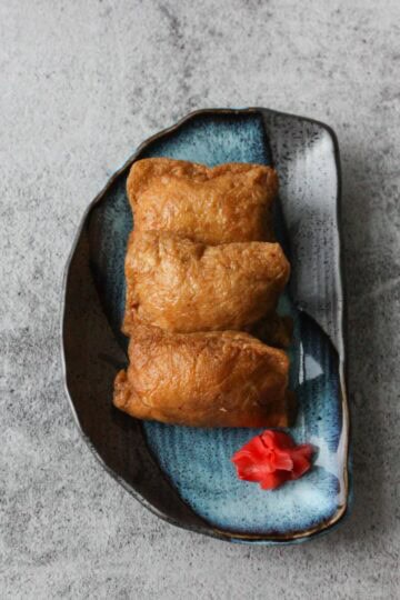 Three inari sushi (inarizushi) on a blue plate.