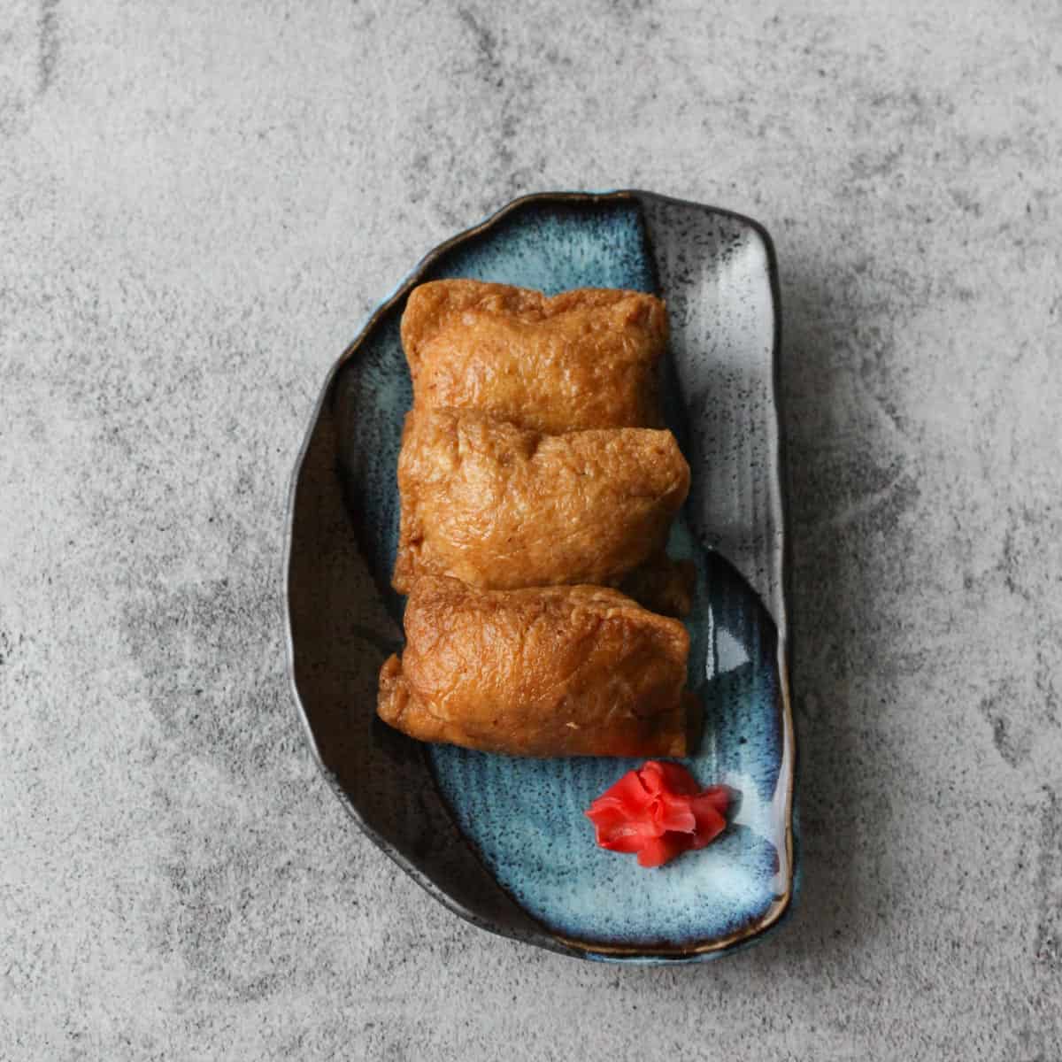 Three inari sushi (inarizushi) on a blue plate.