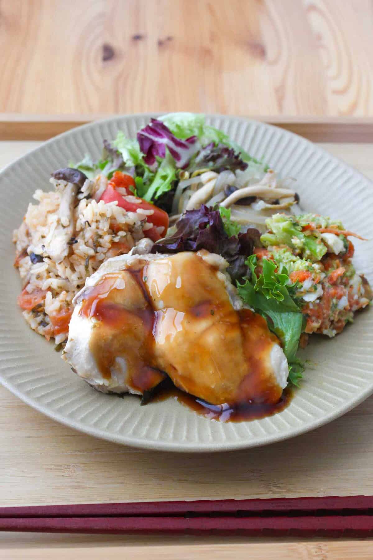 Teriyaki chicken, carrot salad, steamed veggies, and tomato rice on a plate.