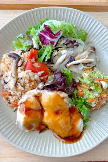 Teriyaki chicken, carrot salad, steamed veggies, and tomato rice on a plate.