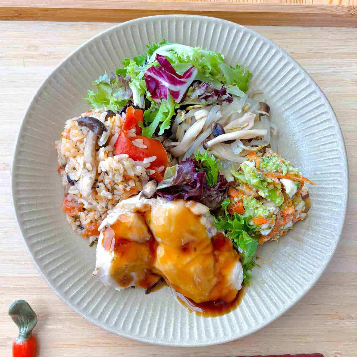 Teriyaki chicken, carrot salad, steamed veggies, and tomato rice on a plate.
