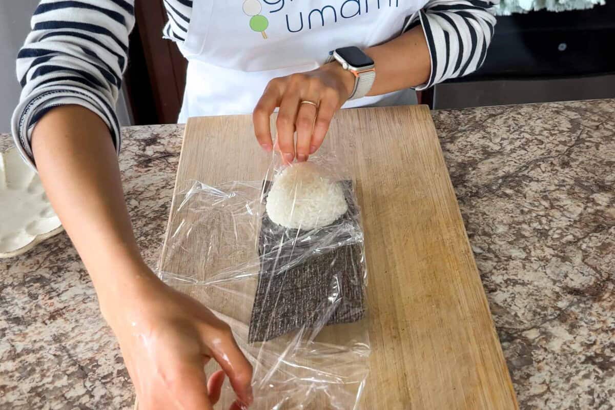 Fold the side of the plastic wrap over the nori and the onigiri.