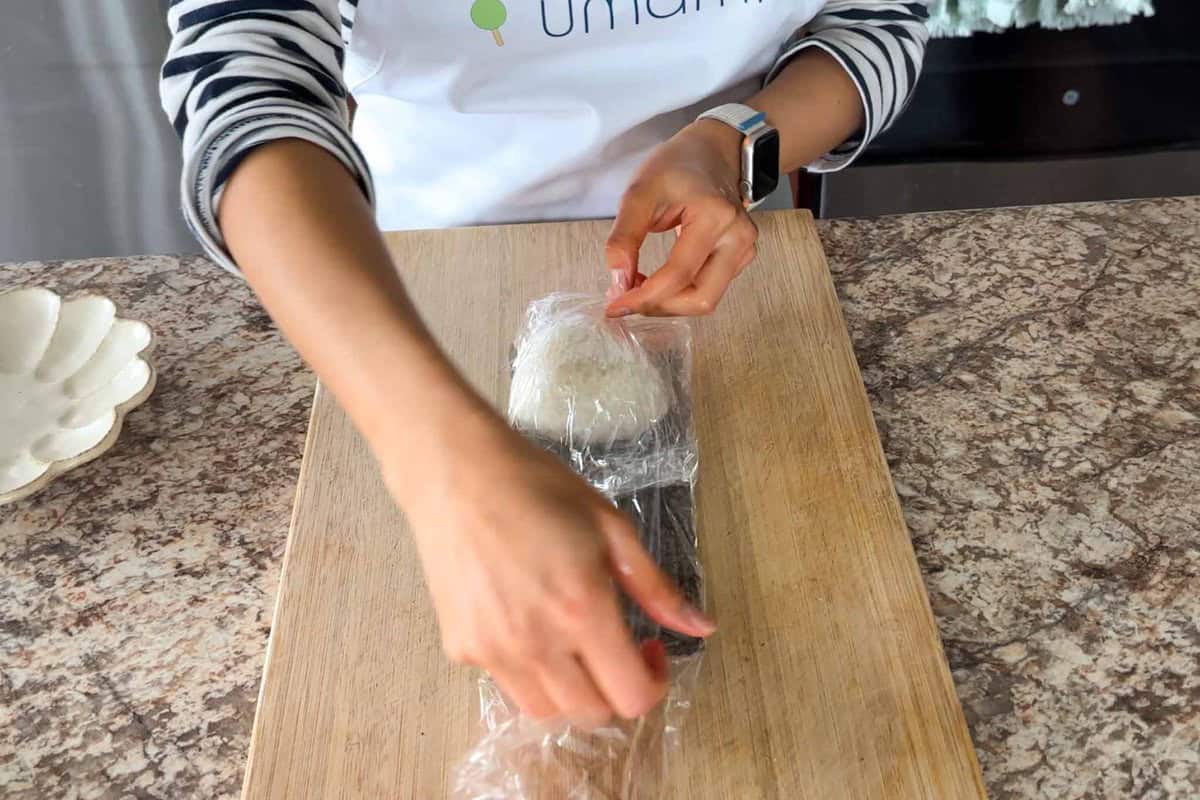 Fold the side of the plastic wrap over the nori and the onigiri.