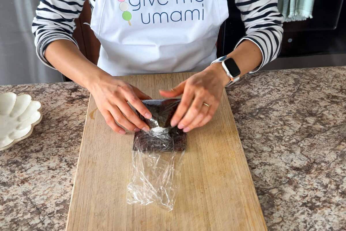 Fold the onigiri with nori over plastic wrap.